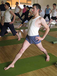 Students in virabhadrasana II in a hall