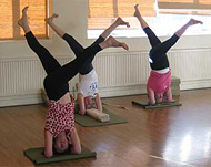 Three students in head stand on mats in a hall